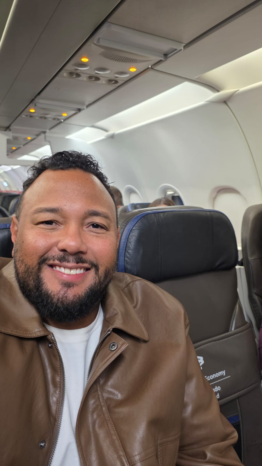 Marcelo Dias sentado na poltrona de um avião, na classe econômica